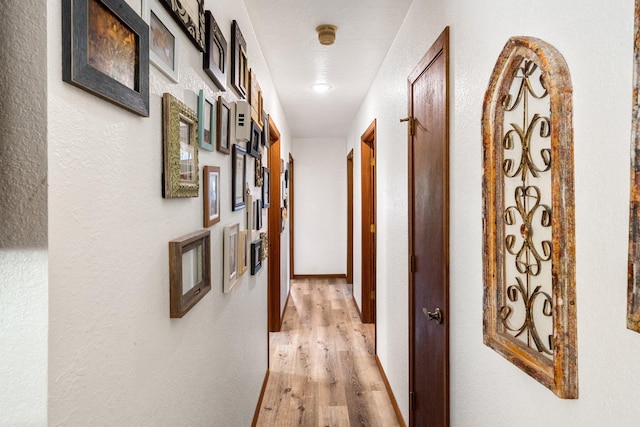 hallway featuring light wood-style floors and a textured wall