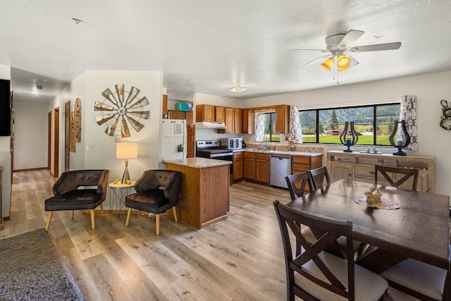 kitchen featuring brown cabinetry, light wood-style flooring, stainless steel appliances, a peninsula, and under cabinet range hood