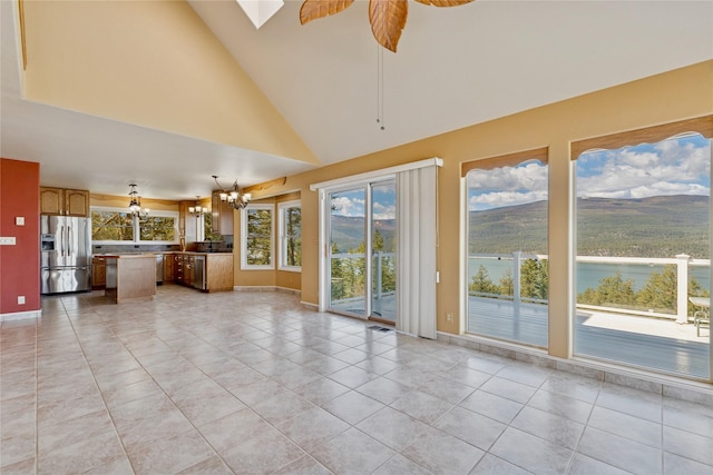 unfurnished living room with baseboards, light tile patterned floors, ceiling fan with notable chandelier, and high vaulted ceiling