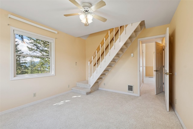 empty room with carpet floors, ceiling fan, baseboards, and stairs