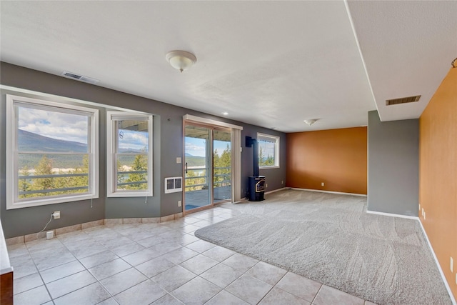 carpeted empty room featuring baseboards, tile patterned flooring, a wood stove, and visible vents