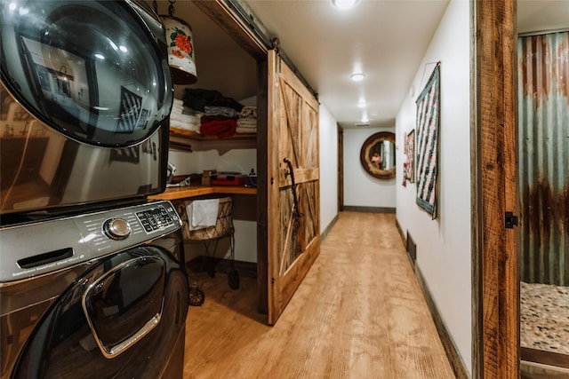 clothes washing area with stacked washer and dryer, laundry area, a barn door, light wood finished floors, and baseboards
