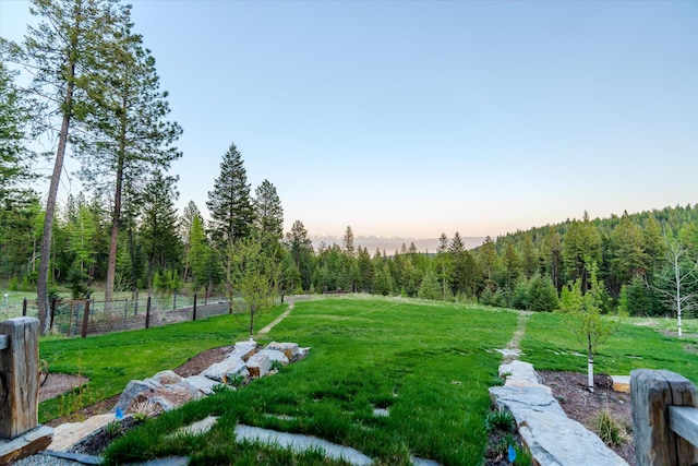 surrounding community featuring a lawn, a forest view, and fence