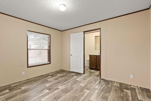 unfurnished bedroom with a textured ceiling, ornamental molding, ensuite bathroom, and wood finished floors