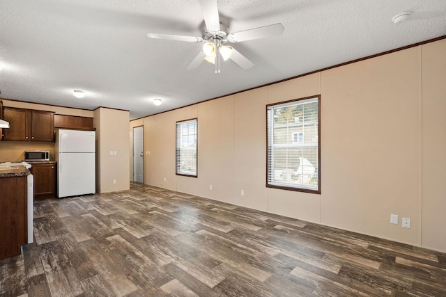 kitchen with a textured ceiling, freestanding refrigerator, a ceiling fan, stainless steel microwave, and dark wood-style floors