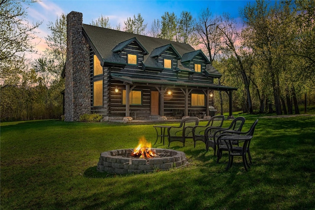 rear view of property with a lawn, a fire pit, and a chimney