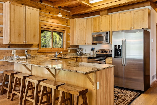 kitchen featuring light brown cabinets, light stone countertops, stainless steel appliances, and a peninsula