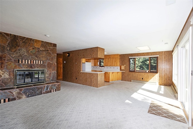 unfurnished living room featuring a fireplace, baseboard heating, wood walls, and light colored carpet