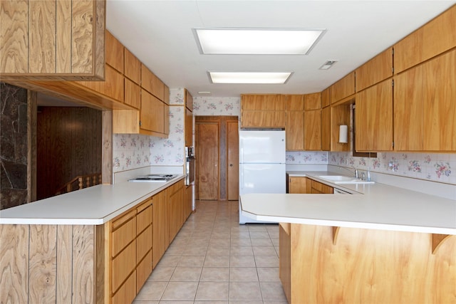 kitchen featuring light countertops, a peninsula, wallpapered walls, and a sink