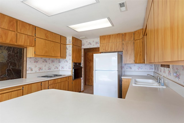 kitchen featuring a sink, electric cooktop, freestanding refrigerator, and wallpapered walls