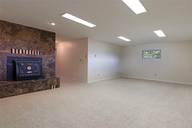 unfurnished living room featuring baseboards, a wood stove, and carpet flooring