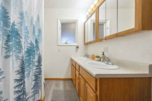 bathroom featuring a sink, baseboards, double vanity, and wood finished floors