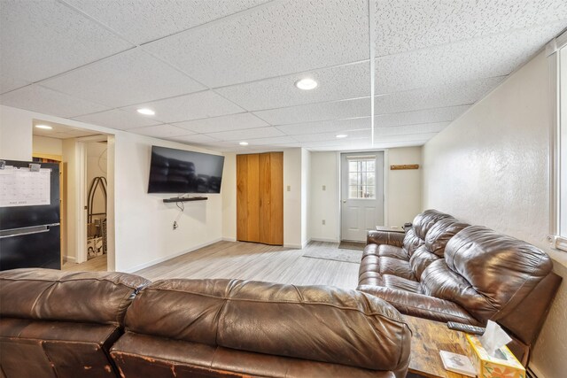 living area featuring baseboards, light wood-style flooring, and a paneled ceiling