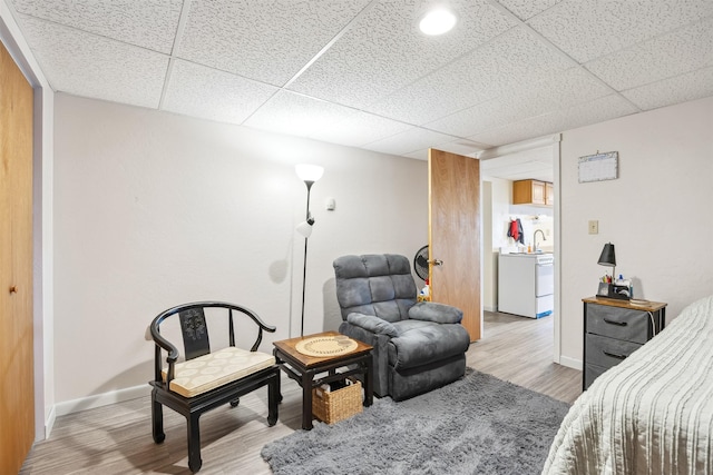 bedroom with washer / dryer, baseboards, light wood finished floors, and a paneled ceiling
