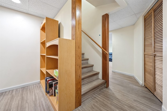staircase featuring baseboards, wood finished floors, and a paneled ceiling