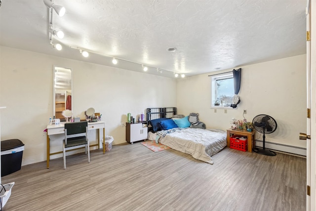 bedroom featuring a textured ceiling, a baseboard heating unit, and wood finished floors