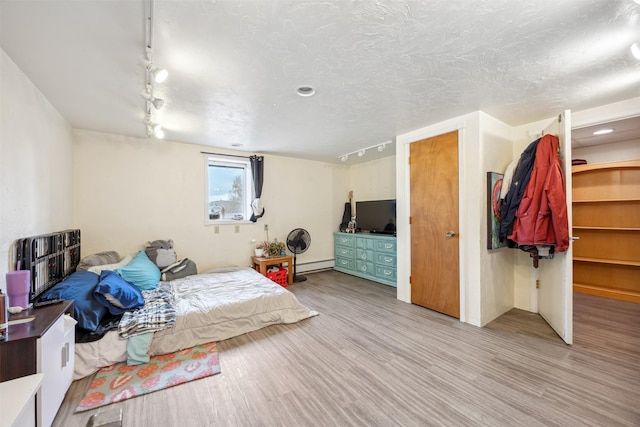 bedroom featuring track lighting, wood finished floors, and baseboard heating