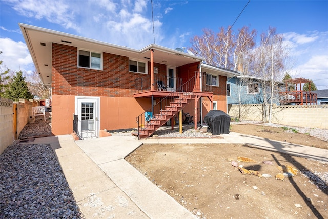rear view of house with fence, stairway, and brick siding