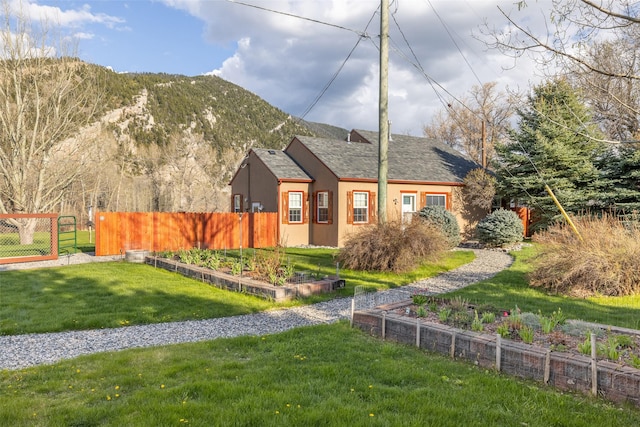 view of front facade featuring fence, a shingled roof, a front lawn, stucco siding, and a mountain view
