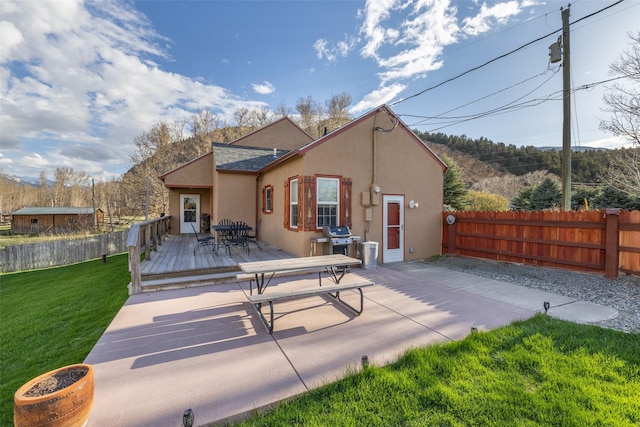 back of house with a wooden deck, a fenced backyard, a yard, a patio, and stucco siding