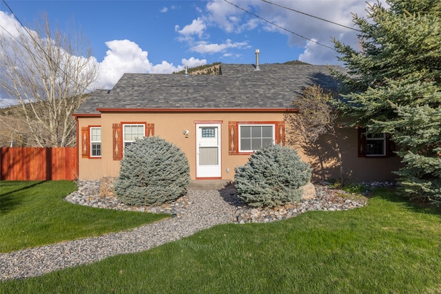 rear view of house featuring a lawn, fence, a shingled roof, and stucco siding