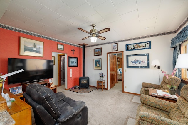 carpeted living area with crown molding, a ceiling fan, baseboards, and a wood stove
