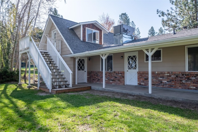 view of front of house with stairway, a shingled roof, a front lawn, and brick siding