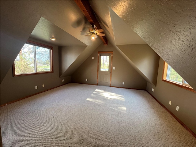 additional living space featuring vaulted ceiling with beams, ceiling fan, a healthy amount of sunlight, and light carpet