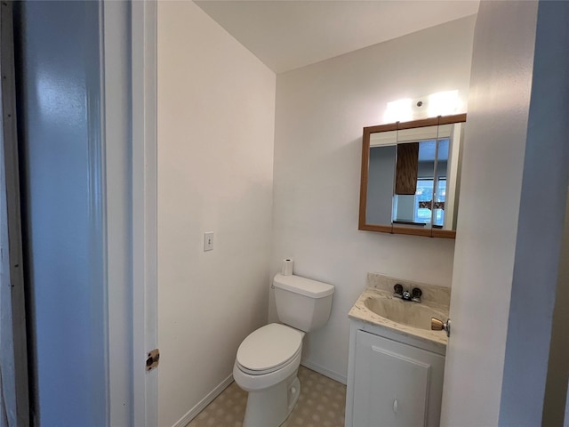 half bathroom with vanity, baseboards, tile patterned floors, and toilet