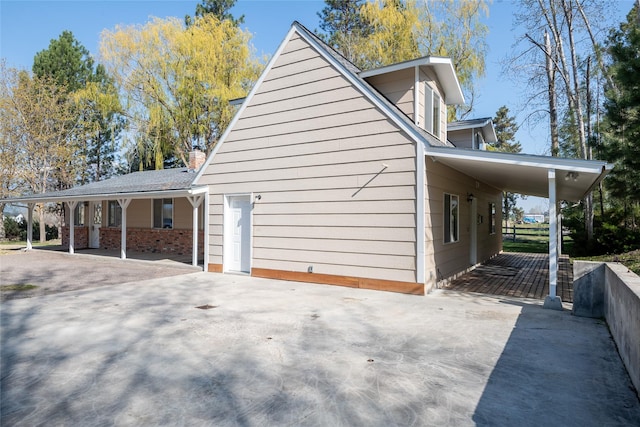 view of property exterior featuring concrete driveway, brick siding, covered porch, and an attached carport