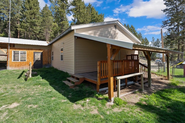 rear view of property with a lawn, a wooden deck, metal roof, and fence