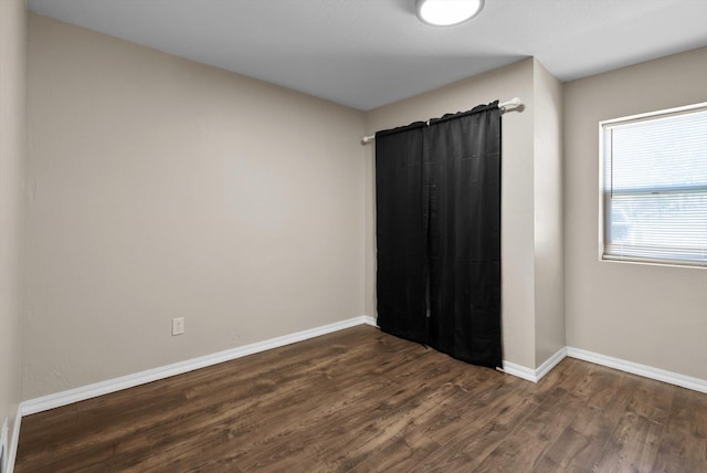 unfurnished room with baseboards and dark wood-style flooring