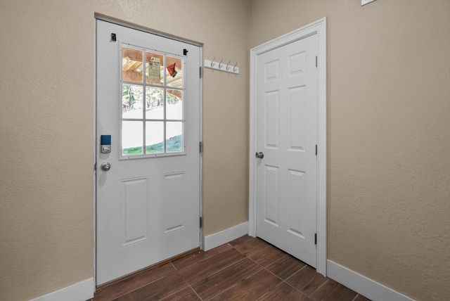 doorway to outside featuring baseboards, a textured wall, and dark wood finished floors