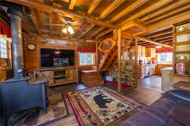 living area featuring wooden walls, beam ceiling, stairs, a ceiling fan, and dark wood-style floors