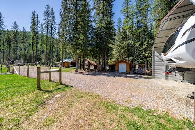 view of yard with a shed, an outbuilding, a forest view, and fence