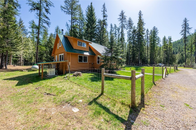 view of home's exterior featuring metal roof, fence, a yard, and a forest view