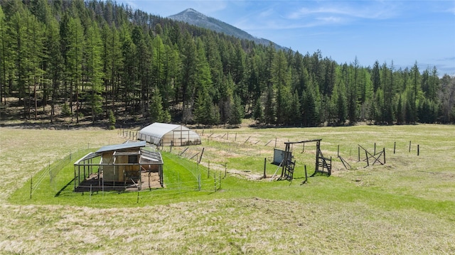 view of yard featuring fence, a wooded view, a mountain view, and an outbuilding