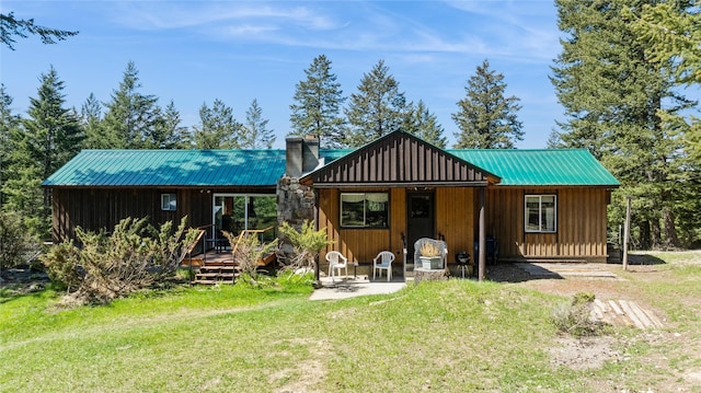 back of property with a deck, a chimney, board and batten siding, metal roof, and a yard