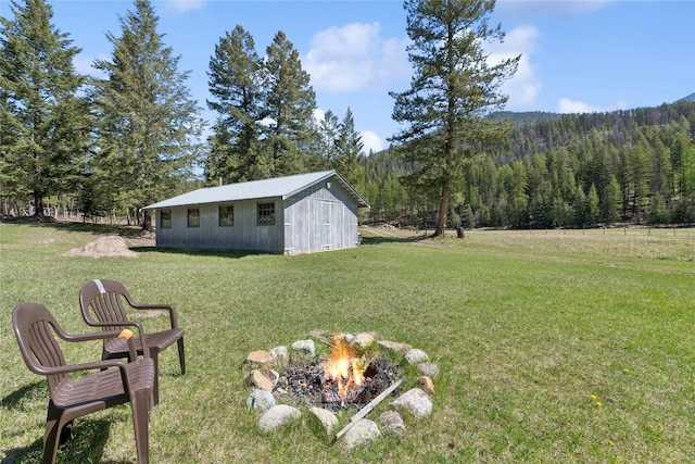 view of yard featuring a fire pit, an outbuilding, and a wooded view