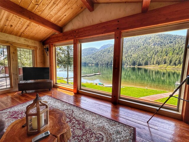 living area featuring a view of trees, hardwood / wood-style floors, and vaulted ceiling with beams