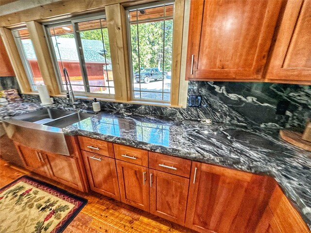 kitchen with stainless steel dishwasher, a wealth of natural light, a sink, wood finished floors, and brown cabinets