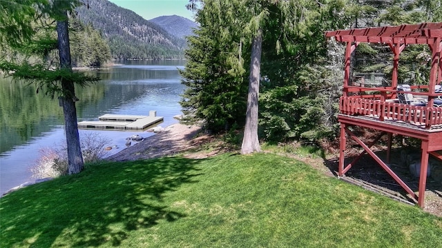 dock area with a lawn, a wooded view, a pergola, and a deck with water view
