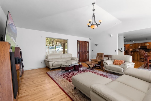 living area with baseboards, a notable chandelier, light wood-style flooring, and vaulted ceiling