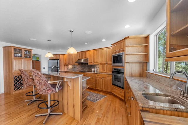 kitchen with under cabinet range hood, brown cabinetry, light wood finished floors, a sink, and stainless steel appliances