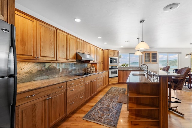 kitchen with black electric stovetop, freestanding refrigerator, open shelves, under cabinet range hood, and light wood finished floors
