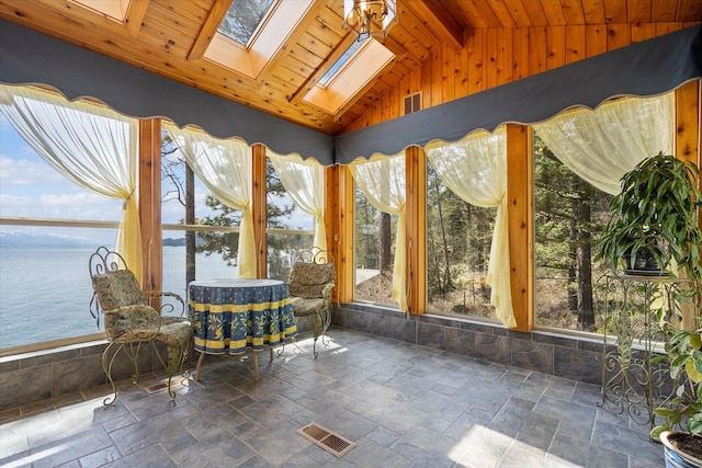 sunroom with stone tile floors, a water view, lofted ceiling with skylight, and visible vents