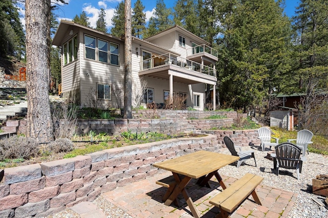 rear view of property featuring a fire pit, a patio area, and a balcony