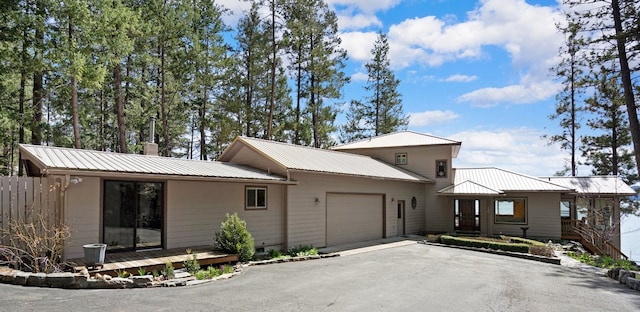 view of front of property featuring an attached garage, a chimney, metal roof, and aphalt driveway