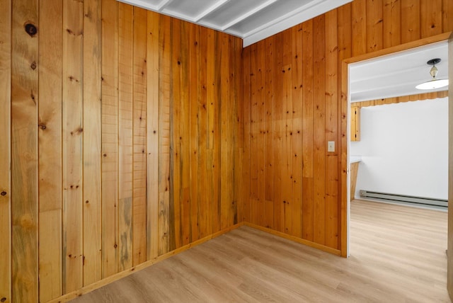 spare room featuring wooden walls, baseboard heating, and light wood-style floors
