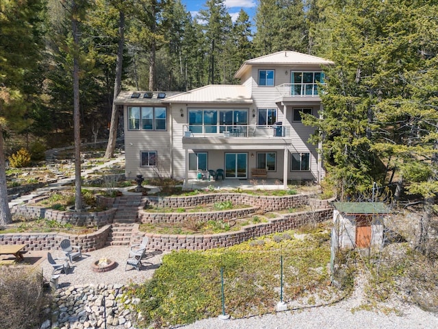rear view of property with metal roof, a patio area, a fire pit, and a balcony